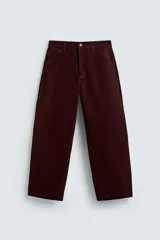 Pantalón de hombre color bordó oscuro, de corte ancho (wide fit), confeccionado en tejido de algodón con acabado flocada o efecto aterciopelado. Presenta cinco bolsillos y cierre frontal con cremallera y botón.