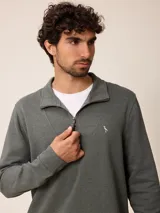 Buzo de polar color verde oscuro, con cuello polo y cierre frontal parcial. Presenta un pequeño bordado en el pecho y puños ajustados.