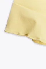 Top negro de cuello halter con lazada, escote recto y hombros descubiertos. Presenta un volante asimétrico en el lateral.