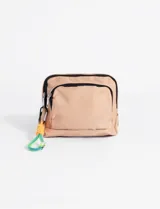 Bolso bandolera pequeño color beige, confeccionado en poliéster con cierre frontal y compartimento principal. Incluye un llavero decorativo de cuerda multicolor con mosquetón.