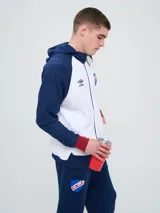Campera deportiva Umbro del Club Nacional de Football, modelo con capucha, cierre frontal, bolsillos laterales y mangas raglán. Diseño en color blanco con mangas y detalles en azul marino y rojo.