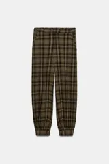 Pantalón bombacho de tiro medio con estampado a cuadros en tonos verde militar, negro y blanco. Presenta bolsillos laterales ocultos, cierre frontal con cremallera y botón, y bajo abullonado con puño y botón.