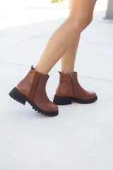 Botas de cuero hechas a mano en color marrón, con diseño de texturas combinadas que incluye cuero liso, gamuza y cuero con grabado tipo animal print en el talón. Poseen suela track de goma negra, cierre lateral interno y tirador trasero.