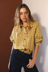 Camisa de manga larga con cuello clásico y cierre frontal de botones. Presenta un diseño de rayas verticales verdes y blancas con un estampado lineal de pequeñas flores rojas.