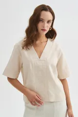 Blusa de viscosa color beige con cuello en V, mangas cortas amplias y detalles de pespuntes decorativos en el frente y las mangas.