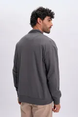 Buzo deportivo gris con cuello alto y cierre frontal parcial, de manga larga y diseño holgado.