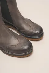 Bota tipo Chelsea de cuero vacuno color suela, con diseño brogue en la puntera y laterales. Presenta paneles elásticos laterales en color marrón oscuro, tirador trasero y suela de goma con plataforma.
