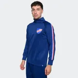 Buzo deportivo de entrenamiento del Club Nacional de Football, color azul, con cuello alto y cierre frontal parcial. Presenta mangas largas con franjas laterales en colores rojo, blanco y azul, y el escudo del club en el pecho.