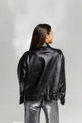 Chaqueta negra de cuero sintético con cuello camisero, cierre frontal con botones a presión, dos bolsillos con solapa en el pecho y puños abotonados.