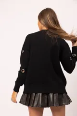 Buzo negro de cuello redondo con detalle de ojalillos metálicos plateados distribuidos en el frente y las mangas. Diseño de corte relajado con terminaciones acanaladas en cuello, puños y ruedo.