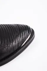 Botín de cuero vacuno negro con textura grabada, taco cuadrado y punta fina con detalle metálico. Presenta una tira decorativa con tachas metálicas y hebilla ajustable alrededor del tobillo.