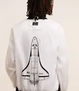 Campera tipo bomber blanca con detalles en negro, inspirada en uniformes espaciales de la NASA. Presenta parches con el logo de la NASA, la bandera de EE. UU. y texto en la manga que dice "Kennedy Space Center".