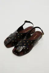 Sandalias planas de cuero sintético marrón, con tiras cruzadas en el empeine y tachas metálicas doradas distribuidas por toda la capellada. Cuenta con tira ajustable en el talón con hebilla.