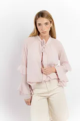 Blusa color rosa pálido de algodón, con cuello alto con lazo y mangas largas con volados.