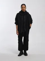 Buzo hoodie oversize de felpa de algodón color gris, con capucha y bufanda integrada que envuelve el cuello. Presenta cierre frontal y bolsillos canguro.