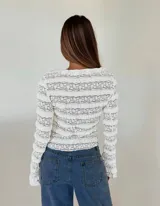 Blusa de encaje blanco con transparencias, escote en V, mangas largas y cierre frontal con finos lazos ajustables.