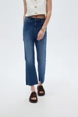 Pantalón jean de corte recto y tiro alto, en color azul, con diseño clásico de cinco bolsillos y terminación desmechada en los tobillos.
