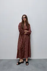 Vestido largo de silueta amplia y caída fluida, con estampado y recortes fruncidos que aportan movimiento. Presenta escote con abertura, cierre frontal con botones y mangas largas de volumen amplio con puños elastizados.