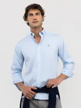 Camisa de hombre de corte regular fit, color celeste, confeccionada en algodón con acabado vintage. Presenta cuello buttondown, cierre frontal con botones, mangas largas con puño simple y logo bordado en el pecho.