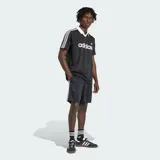 Camiseta Adidas Originals de manga corta, color negro con sutiles rayas verticales, cuello polo en V de color blanco, al igual que las líneas características de la marca en los hombros. Cuenta con el logotipo de la marca y la inscripción "adidas" en el pecho en color blanco.