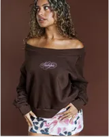 Buzo de cuello bote estilo off-shoulder, color marrón, con mangas largas y estampa bordada con la palabra Nostalgia en el frente.