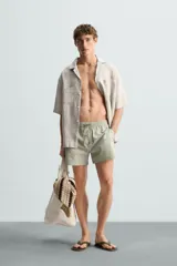 Bañador de hombre color verde claro con finas rayas blancas verticales (efecto seersucker). Tiene cintura elástica ajustable con cordón verde, bolsillos laterales y un bolsillo trasero de vivo.