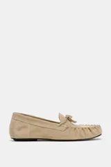 Mocasín plano de serraje color beige, con detalle de fruncido y lazo en la parte delantera y punta redonda.