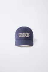 Gorra de béisbol azul marino con visera curva y detalle de borde en color crema. Presenta un bordado frontal con la palabra 'LONDON' en tipografía estilo varsity y texto adicional debajo.
