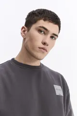 Buzo de algodón con calce oversize, cuello redondo, mangas largas con puños y bolsillos laterales. Presenta un parche cuadrado negro con lettering en el pecho y detalle de estampado en el ruedo.