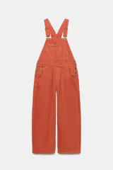 Mameluco de denim color naranja con tirantes ajustables, bolsillos de plastrón en el pecho y bolsillos laterales. Cuenta con cierre de ganchos metálicos en el delantero y botones en los laterales.