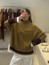 Buzo tejido de punto con cuello alto, diseño holgado y aberturas laterales. Presenta un cuerpo en color azul melange con detalles de franjas en color crema y verde en los puños y el ruedo. Incluye un pequeño bordado en el pecho.