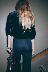 Top corto de velour negro, con cuello mao y botones forrados. Presenta canesú fruncido en la parte delantera y trasera, mangas abullonadas al codo y ribete fino en puños y bajo.