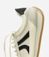 Championes estilo runner de diseño vintage, confeccionados en una combinación de tejido de malla respirable, recortes de gamuza y detalles en material sintético. Presentan cierre con cordones, detalle lateral aplicado en contraste y suela de goma plana con base color caramelo.
