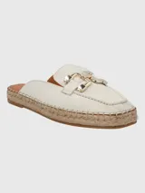 Sandalia tipo mule con base de yute estilo alpargata, confeccionada en cuero color blanco. Presenta una puntera redonda y un detalle decorativo metálico en tono dorado sobre el empeine.