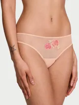 Panty tipo bikini confeccionado en malla elástica de tono rosado, con detalles de ribete picot y un delicado parche bordado de rosas en la parte frontal.