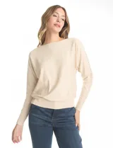 Buzo tejido color beige de manga japonesa, con detalle de tachas metálicas a lo largo de las mangas. Presenta puños y ruedo acanalados.