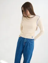 Polera de manga larga confeccionada en tela rib color bordó, con cuello alto y hombreras. Presenta costuras a la vista con pespuntes en hilo de color contrastante en el cuello, puños, hombros y ruedo.