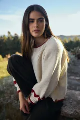 Sweater de punto color crudo con diseño de corazones rojos en las mangas, cuello redondo y terminaciones acanaladas en contraste rojo.