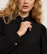 Camisa de crepé color blanco, con cuello inglés, manga larga abullonada con puños abotonados y cierre frontal oculto con botón diferenciado en el cuello.
