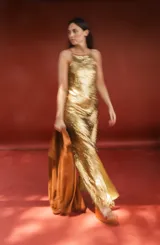 Vestido largo dorado con lentejuelas, silueta recta y fluida, escote halter y finos tirantes de cuero.