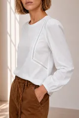 Remera blanca de manga larga con detalles de encaje en el frente y puños elásticos.