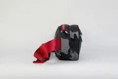 Riñonera de nylon con estampado camuflado en tonos grises y negros. Presenta un bolsillo frontal con cierre, el logo de los Chicago Bulls y una correa ajustable de color rojo con el nombre del equipo grabado.