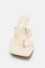 Sandalia de tacón fino medio, color blanco off-white, con diseño de tiras tipo thong para el dedo y punta cuadrada.