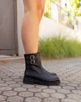 Botas de caña media en cuero negro, con suela track gruesa y dos correas laterales con hebillas metálicas doradas.