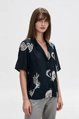 Camisa de algodón con estampado en tonos claros sobre base azul oscura, cuello solapa, mangas cortas y cierre frontal con botones.