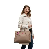 Cartera mediana tipo shopper color marrón, con doble asa de hombro y cierre superior. Incluye un dije colgante con forma de labios y logo de la marca en color fucsia.