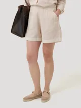 Short de tiro alto con diseño a rayas verticales en tonos beige y blanco. Presenta bolsillos laterales y un dobladillo ancho en la parte inferior.