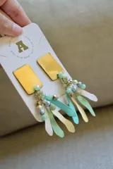 Aros colgantes con base rectangular dorada y cuentas de cristal en tonos celeste, verde y blanco.