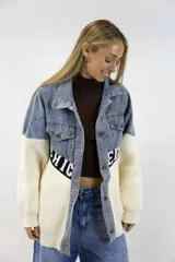 Campera oversize combinada de denim azul en la parte superior y tejido de punto blanco en la parte inferior, con una franja negra con letras blancas en el centro. Cuenta con cierre frontal de botones metálicos y bolsillos en el pecho.