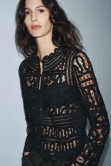 Blusa negra de manga larga confeccionada en tejido tipo crochet con intrincados patrones geométricos y florales. Presenta cuello redondo y cierre frontal con botones.